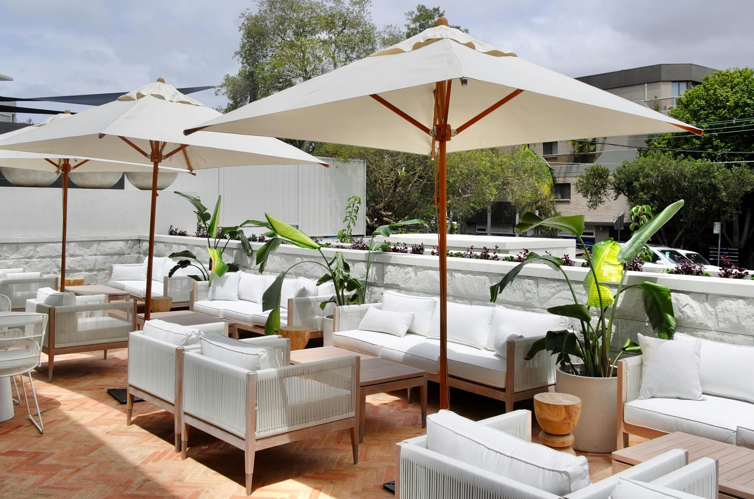 Spacious rooftop lounge featuring modern furniture and green potted plants under large umbrellas.