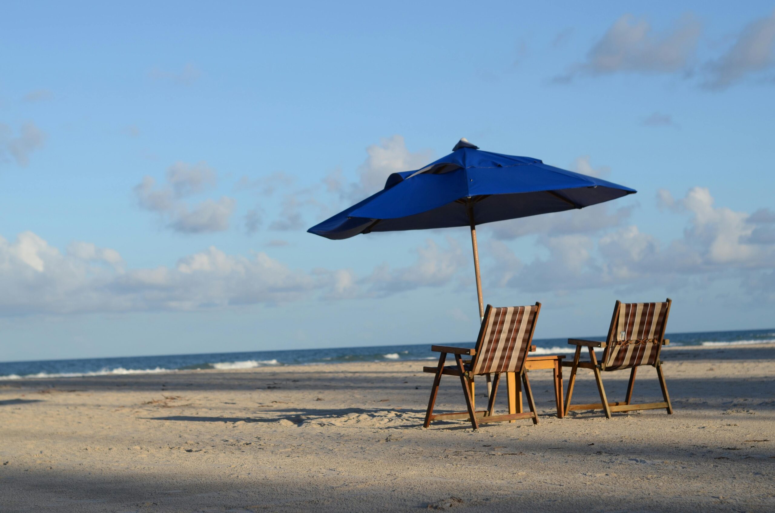 Serene beach with empty chairs and umbrella under a clear blue sky.