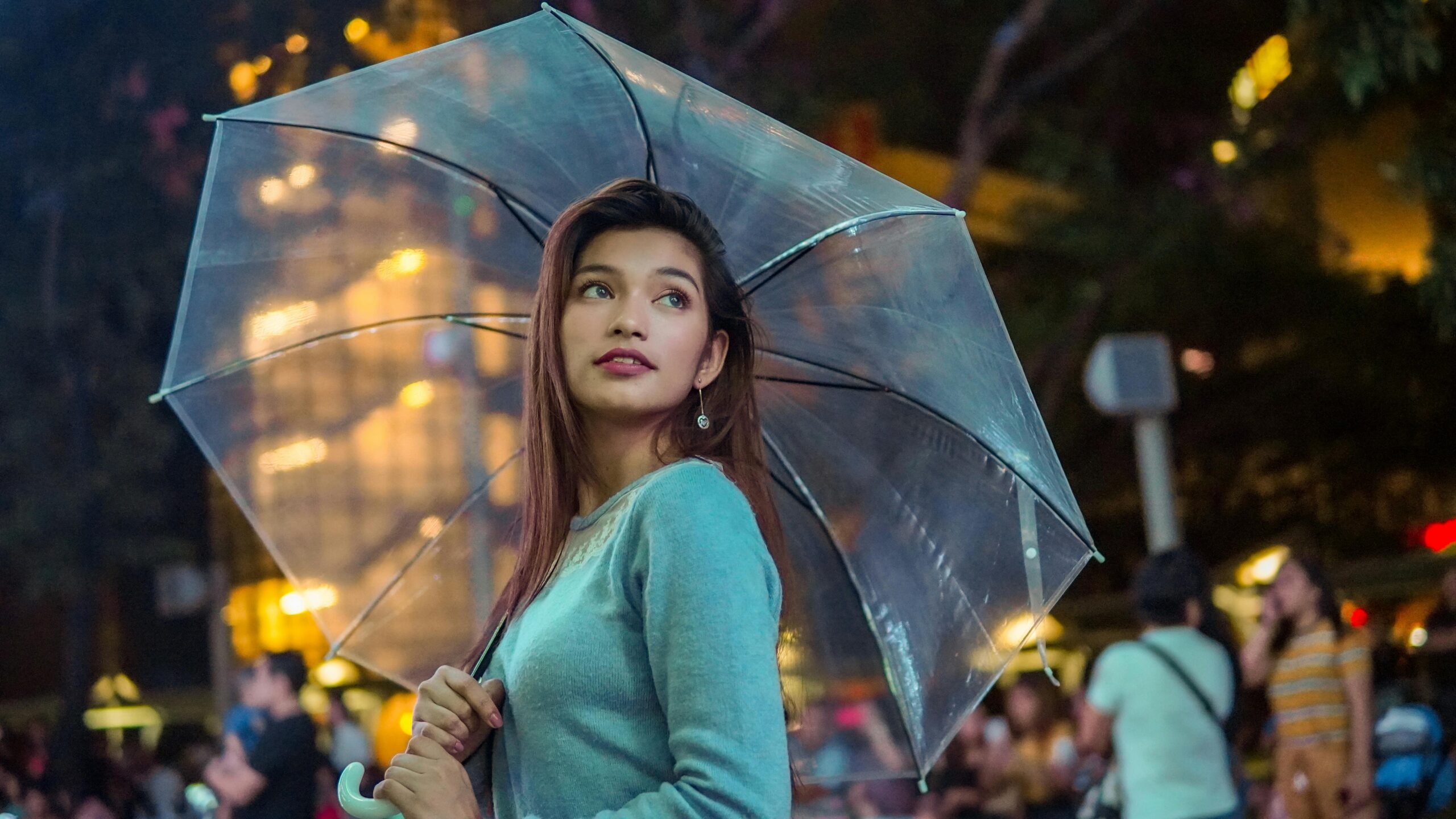 Elegant woman holding a clear umbrella in an urban night setting.