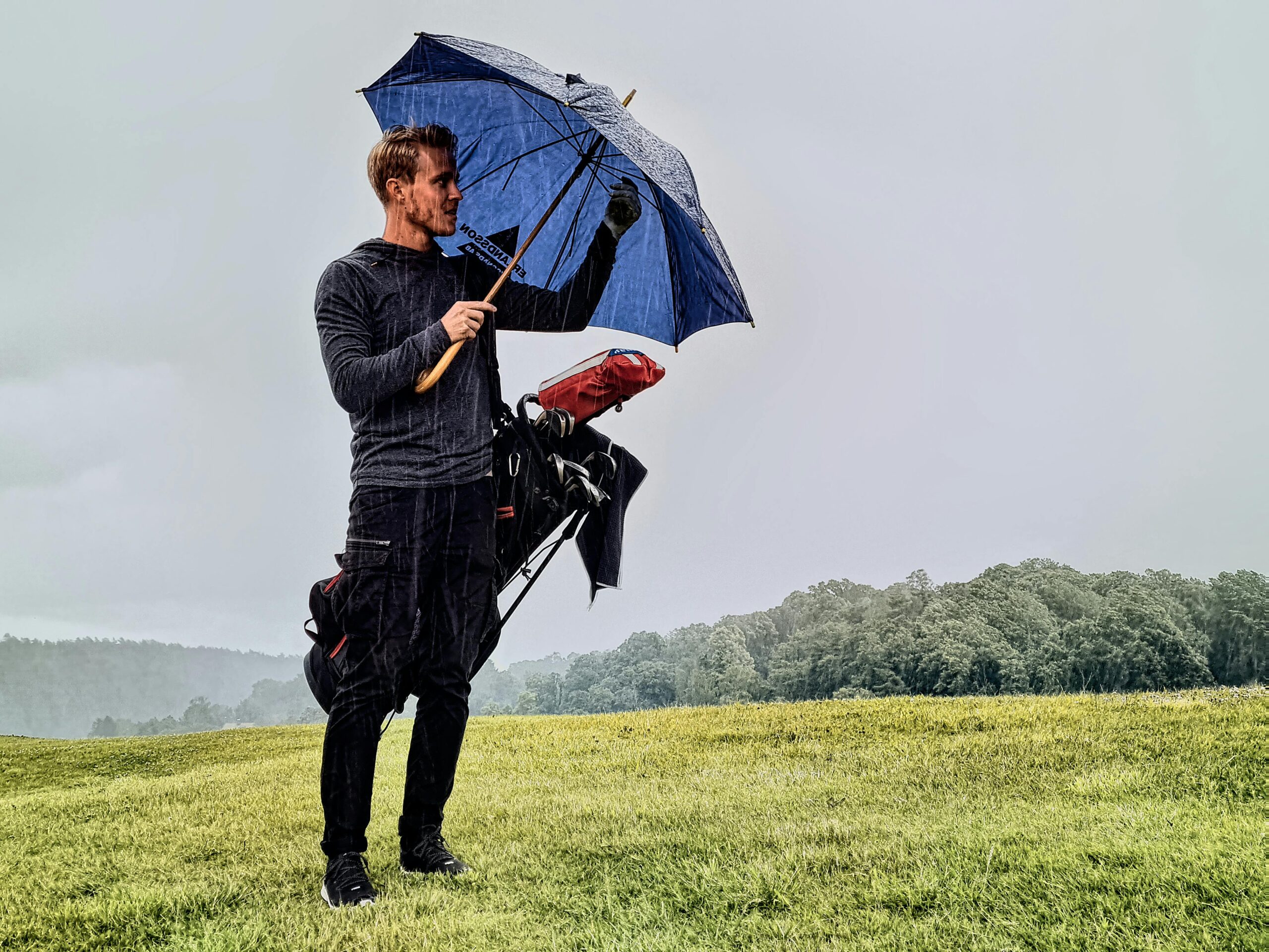 Golf player holding an umbrella while standing on a rainy golf course in Sweden.
