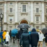 People with umbrellas in rain outside Trinity College Dublin.