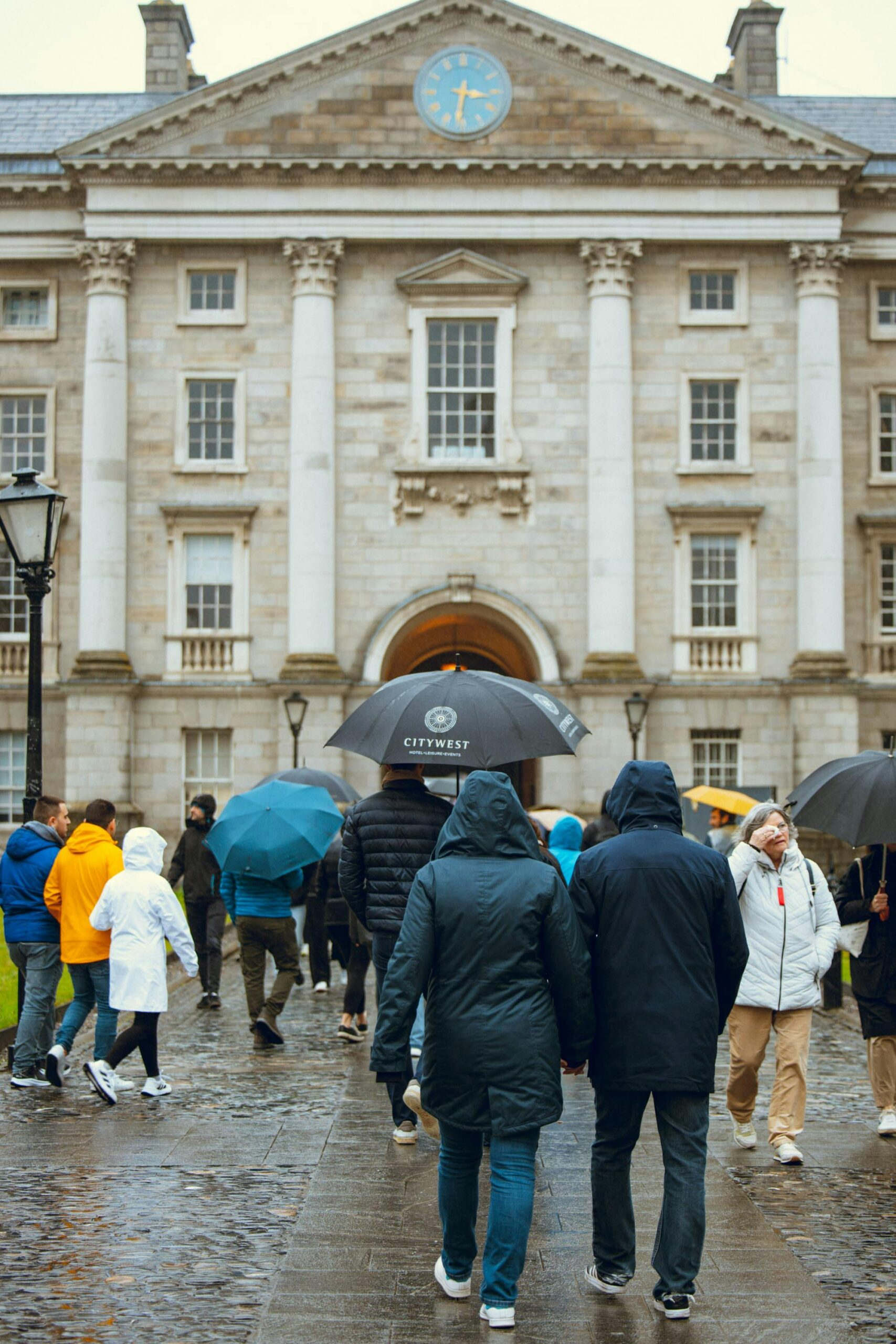 People with umbrellas in rain outside Trinity College Dublin.