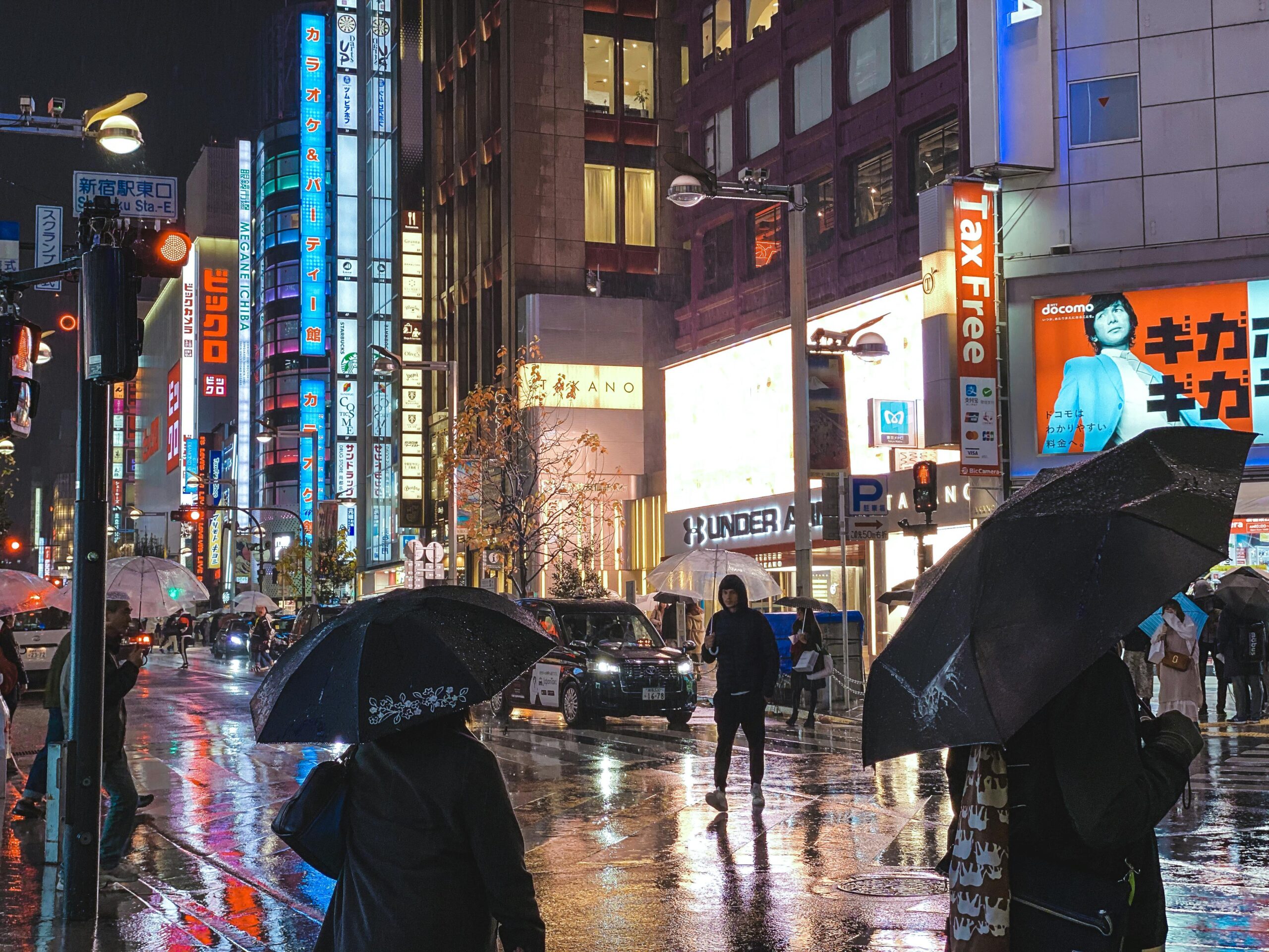 Vibrant city street in Tokyo with neon lights reflecting on wet pavement during a rainy night.